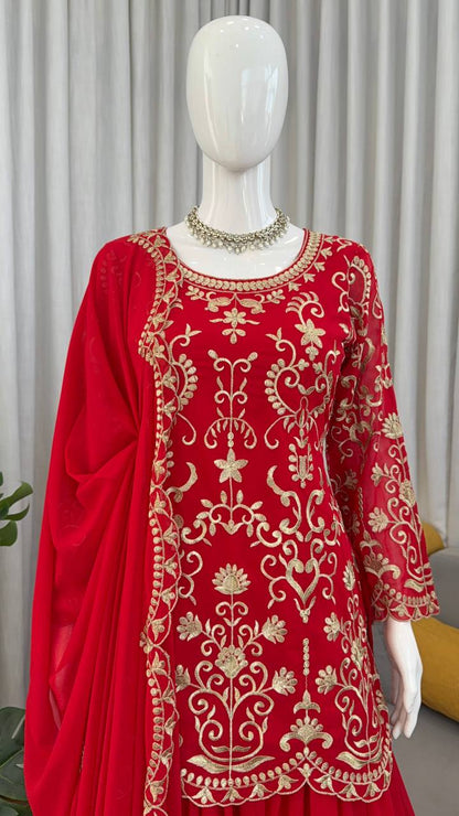 Flat lay of a red pakistani suit dress with gold thread embroidery, matching sharara, dupatta, and mirror-work juttis on a white fur background.