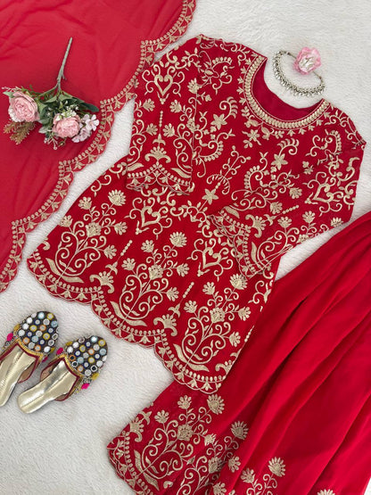 A woman modeling a red pakistani suit dress featuring heavy gold embroidery on the neck and sleeves, paired with large gold earrings and a maang tikka.